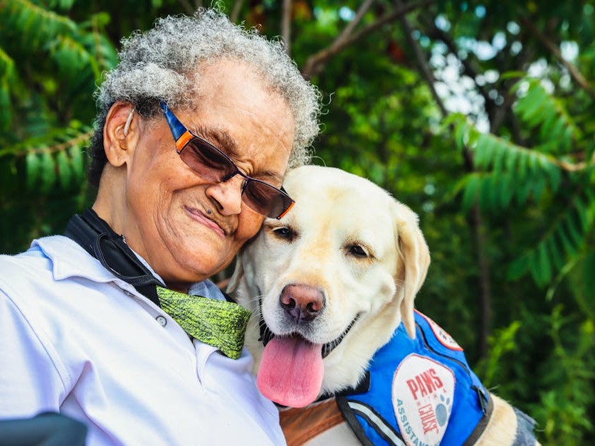 A kupuna hugging a service dog in a blue vest